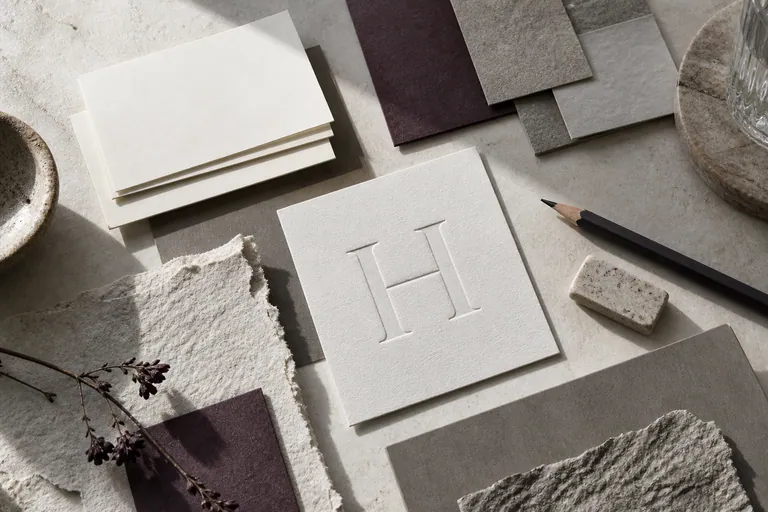 Textured identity samples with an embossed letter H and muted plum paper.